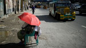 Eine Straßenverkäuferin schützt sich in Manila mit einem Regenschirm vor der Sonne. Foto: Aaron Favila/AP/dpa
